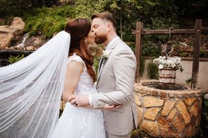 Bride and groom sharing romantic kiss near stone well with flowing wedding veil.