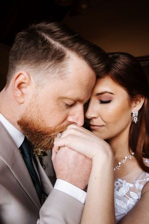 Groom gently kissing bride's hand in an intimate close-up wedding portrait.