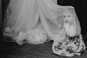 Curious baby peeking out from under the bride's white tulle wedding gown.