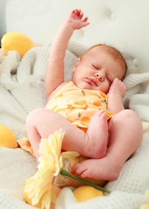 Peaceful newborn baby in yellow onesie stretching arm while sleeping among flowers and lemons.