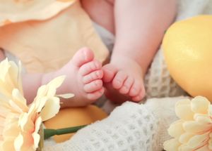 Close-up of tiny newborn baby feet surrounded by soft yellow flowers and pastel decorations.