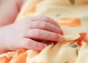Close-up of a newborn baby's tiny hand resting on a soft yellow floral blanket.