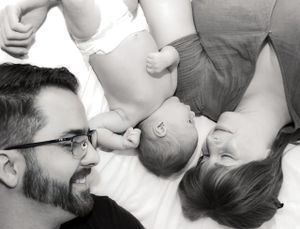 Black and white photo of parents lying down smiling at their newborn baby between them.