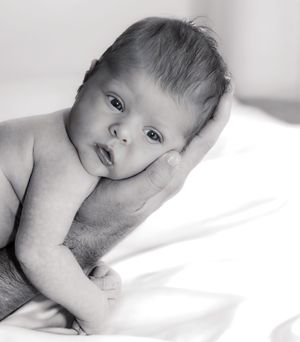 Black and white portrait of a newborn baby being gently supported by an adult hand.
