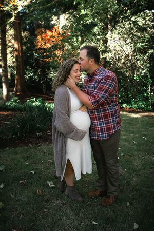 Man kissing pregnant woman on the cheek while embracing her in a beautiful outdoor garden setting.