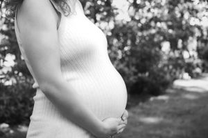 Black and white close-up of a pregnant woman cradling her baby bump outdoors in a park.