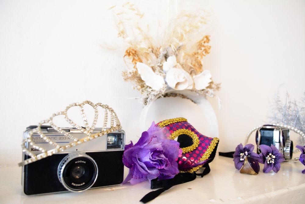 Still life with vintage camera, purple masquerade mask, and elegant accessories.