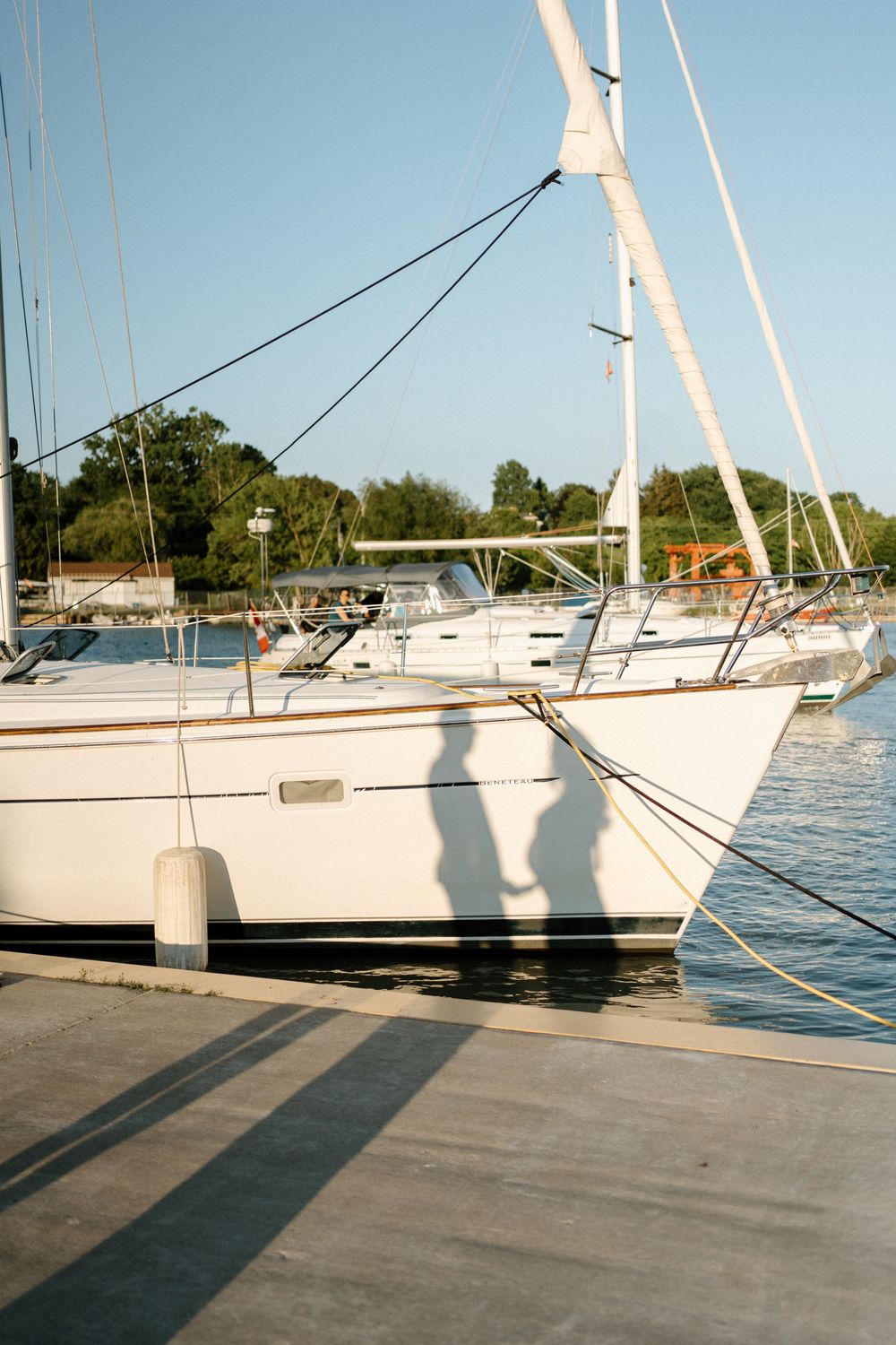 White sailboat docked at a marina with shadows of a couple cast on the dock at golden hour.