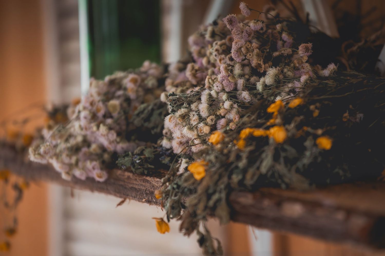 Dried flowers and orange blossoms hang from a wooden beam in rustic farmhouse decor style.