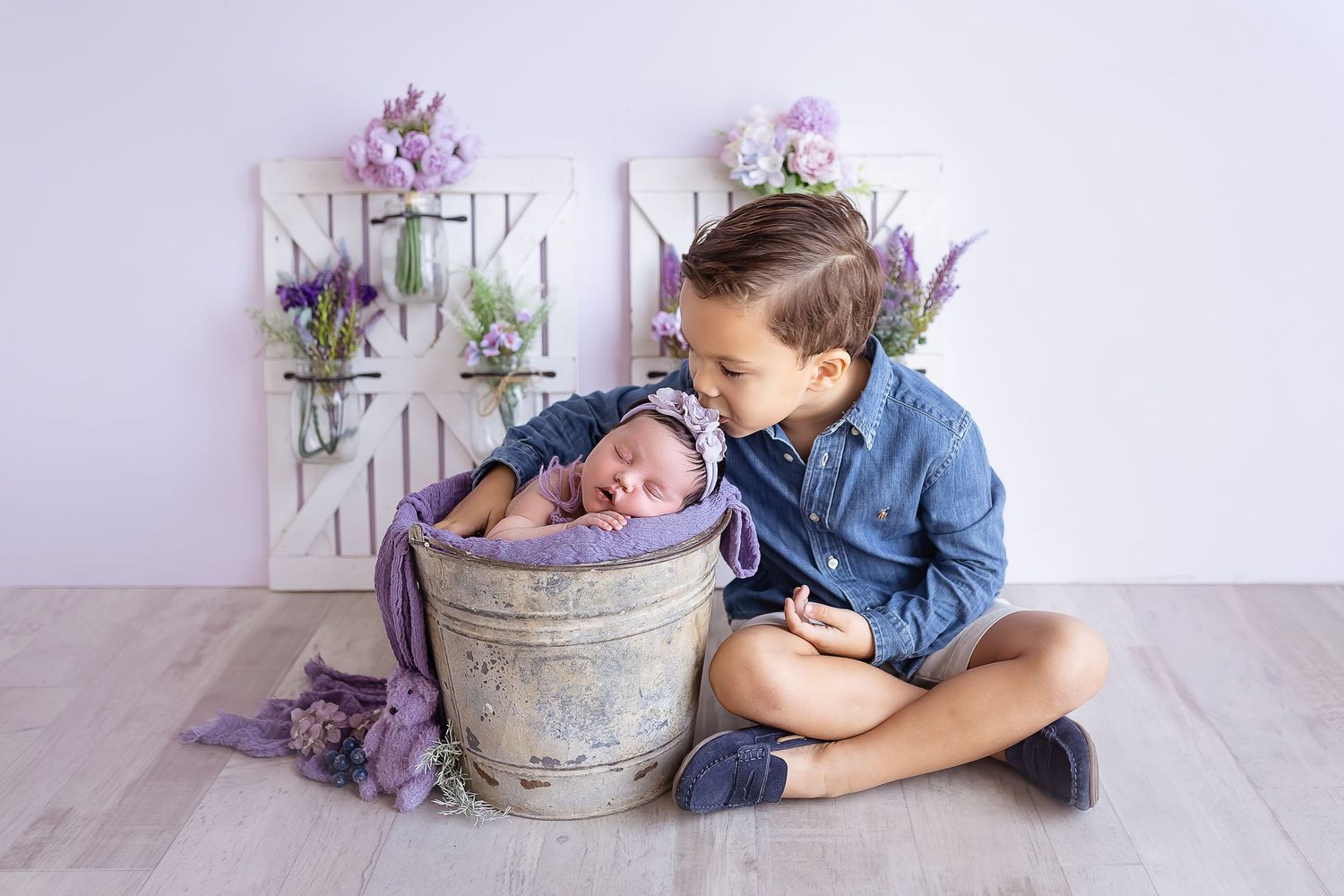 big brother kissing his newborn sisters delicate little head baby is inside a milk bucket