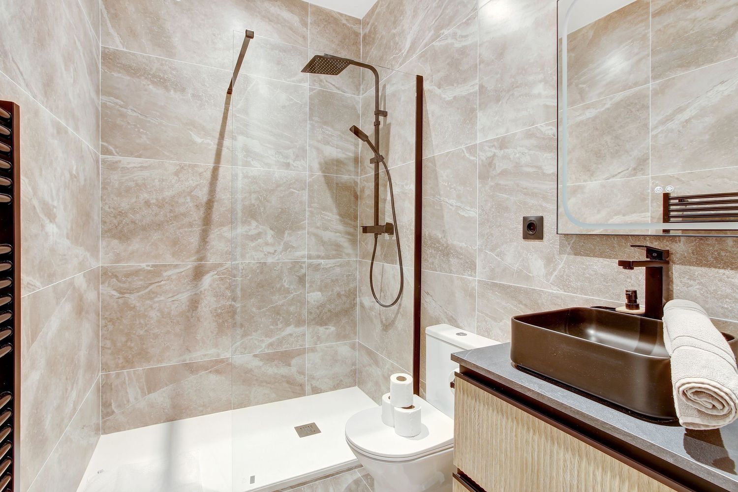 Modern marble-tiled bathroom with walk-in shower, square black sink, and heated towel rail.