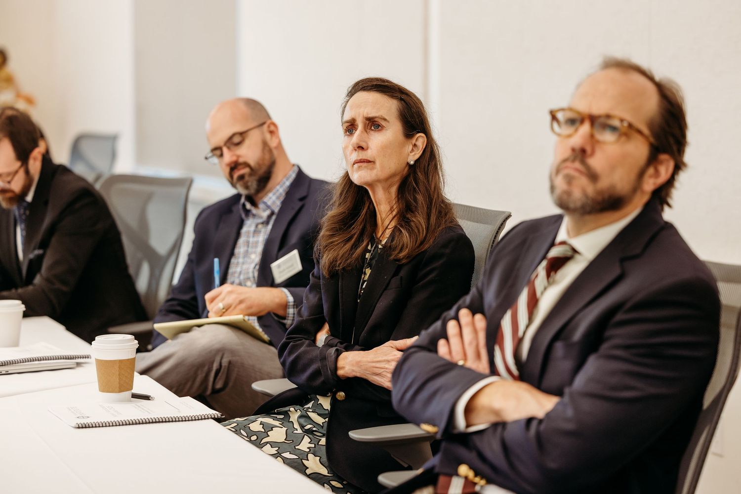 Business professionals sit at a conference table during a meeting in a modern office setting.