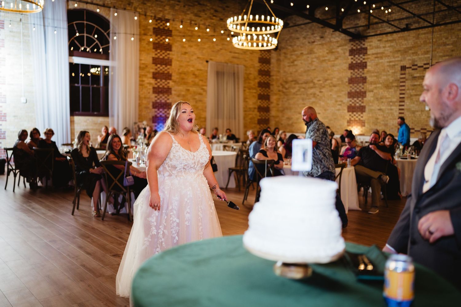 A couple shares their first dance at a wedding reception in an elegant venue with exposed brick walls and string lights.