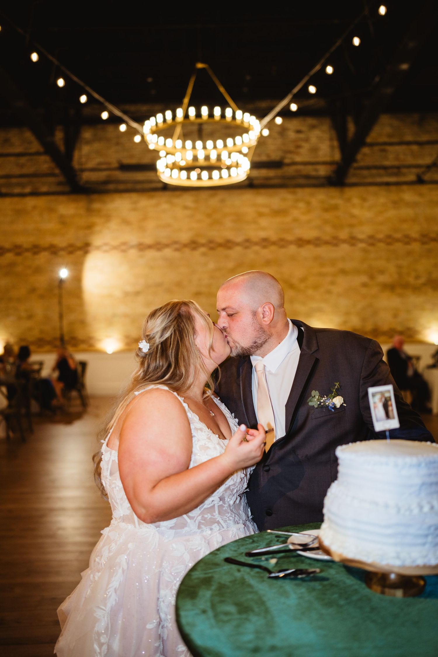 A romantic wedding cake cutting moment in a rustic venue with string lights and exposed brick walls.