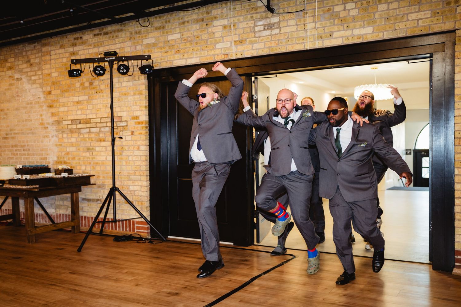 Wedding party performs synchronized dance routine in rustic brick-walled venue during reception celebration.