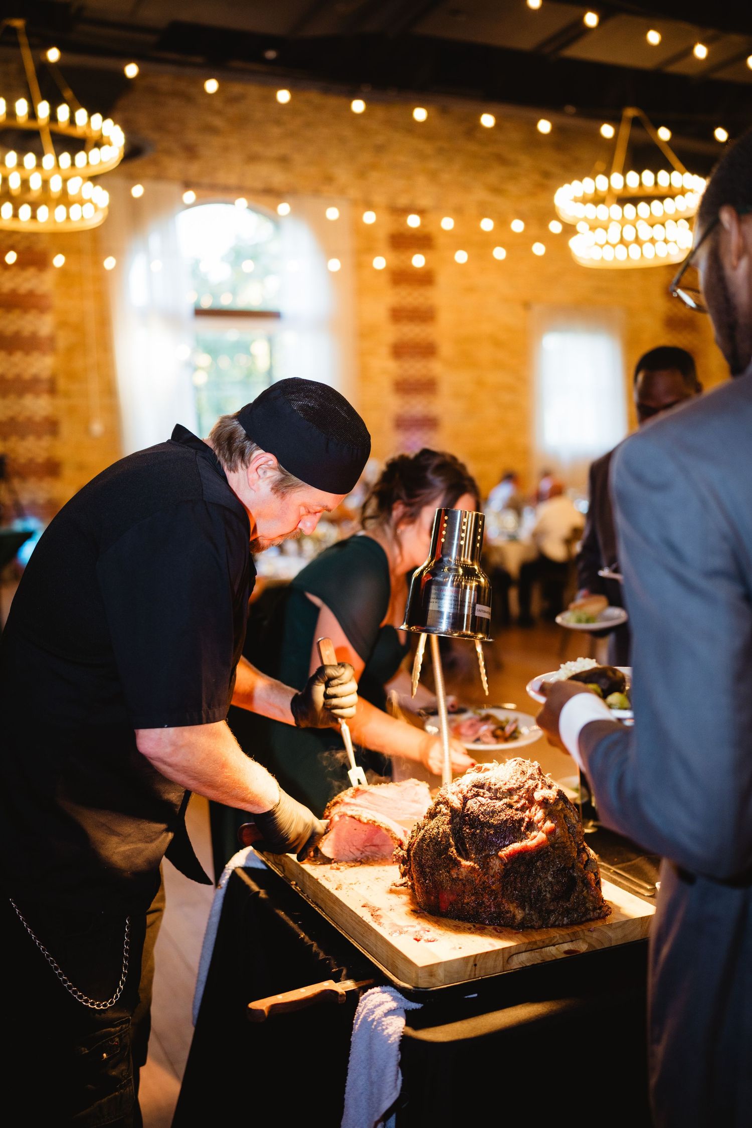 Wedding caterers preparing and serving food at an elegant indoor reception with ambient lighting.