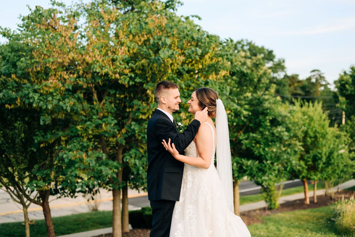 Couple in wedding attire shares romantic moments in a scenic garden setting with lush green trees and natural lighting.