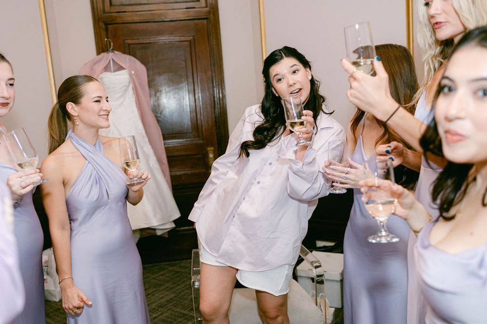 Group of women in light colored dresses and tops celebrating with champagne glasses at a party.