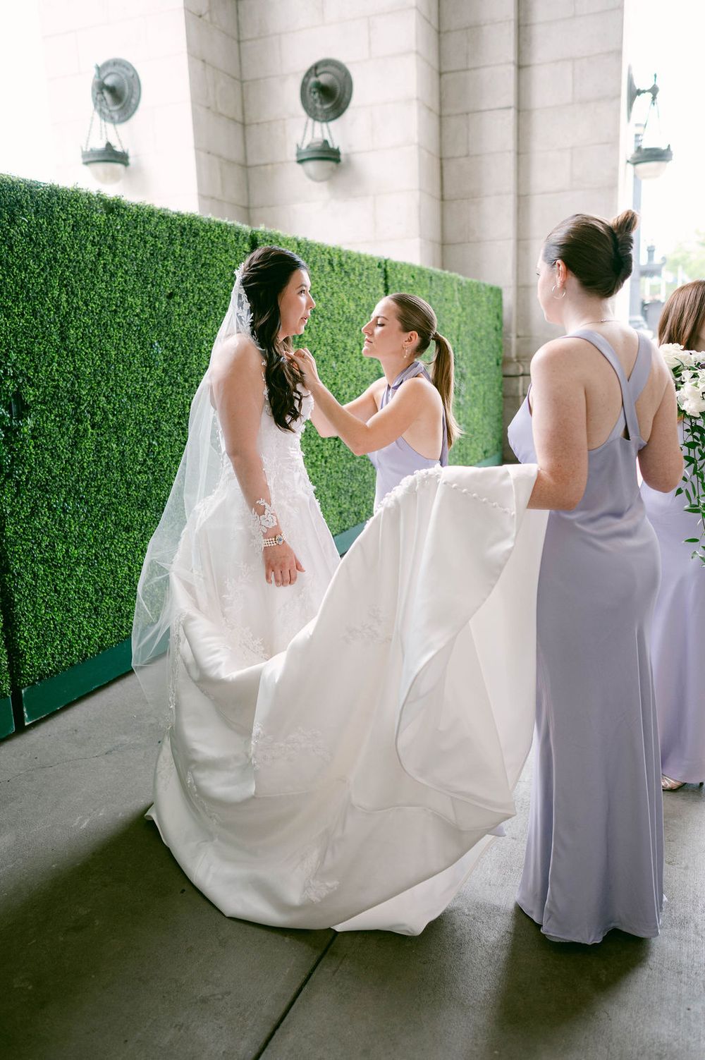 A series of photos showing bridesmaids in lavender dresses helping adjust a bride's white wedding gown outdoors.
