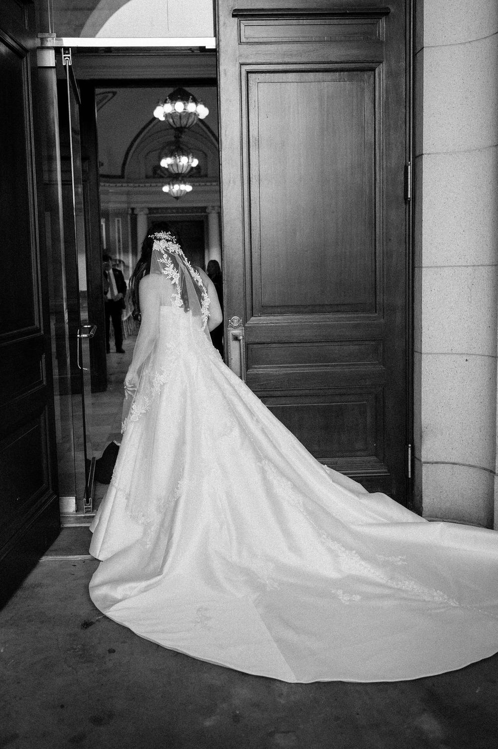 A dramatic black and white photo of a wedding dress with a long cathedral train in an elegant hallway.