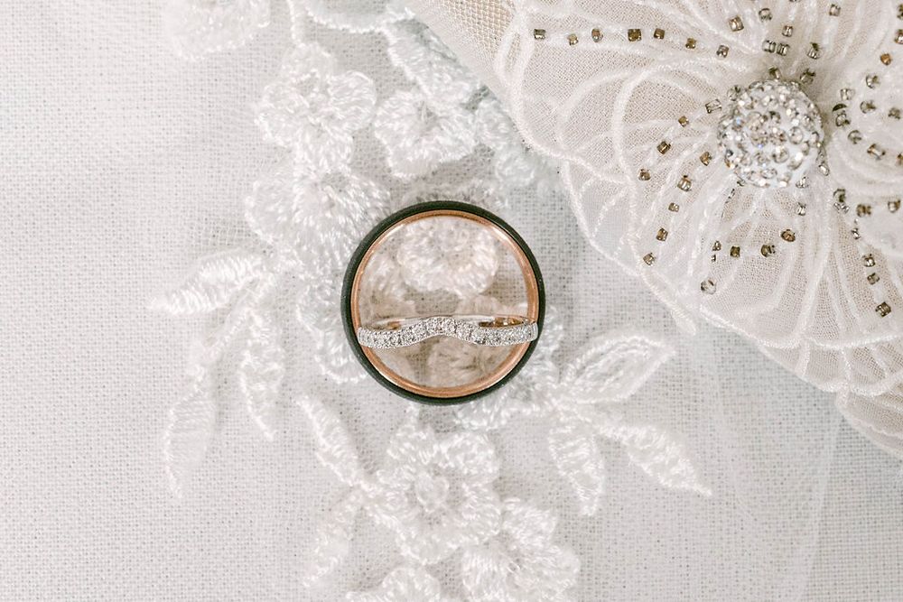 Delicate white lace and wedding rings arranged on light fabric background.