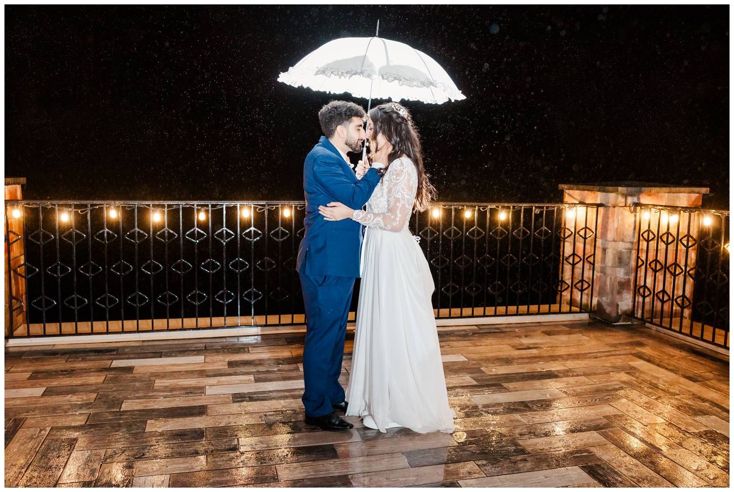 Romantic nighttime wedding photos on a terrace with umbrella and string lights.
