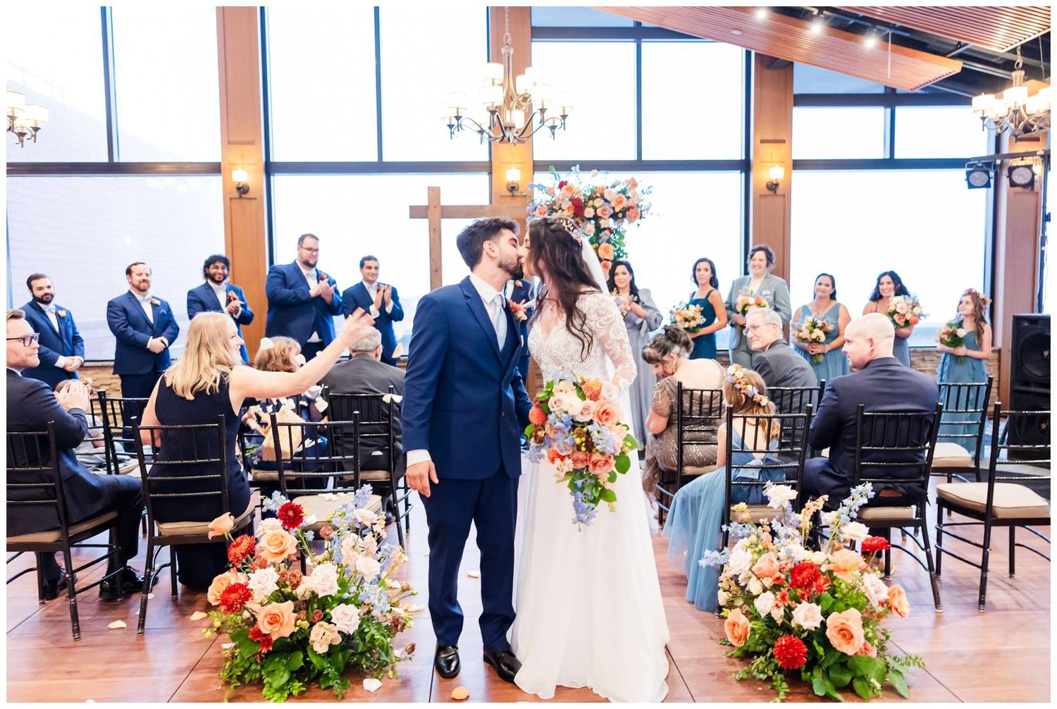 Elegant wedding ceremony setup with floral arrangements and wooden beams in a bright indoor venue.