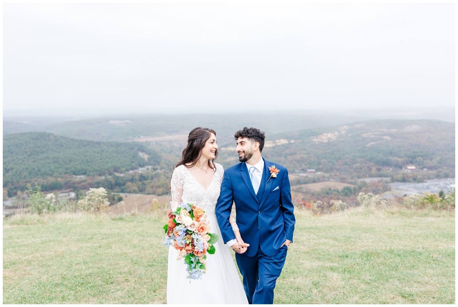 A couple stands together on a hilltop overlooking a scenic autumn landscape.