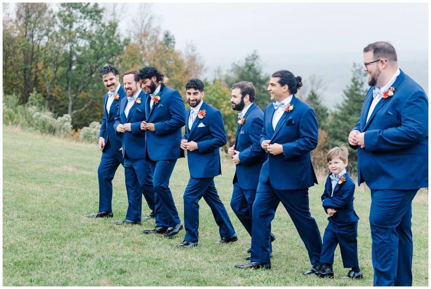 Groomsmen in navy suits having fun and posing together on a hilltop.