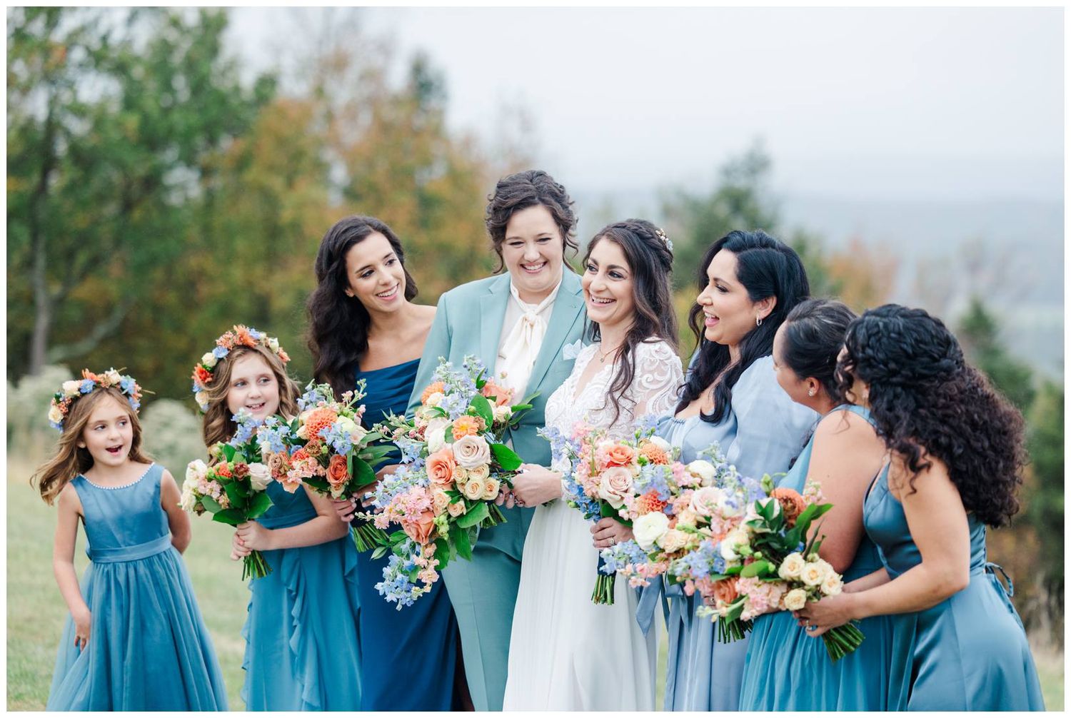 Wedding party members in teal blue dresses pose with colorful coral and peach bouquets outdoors.