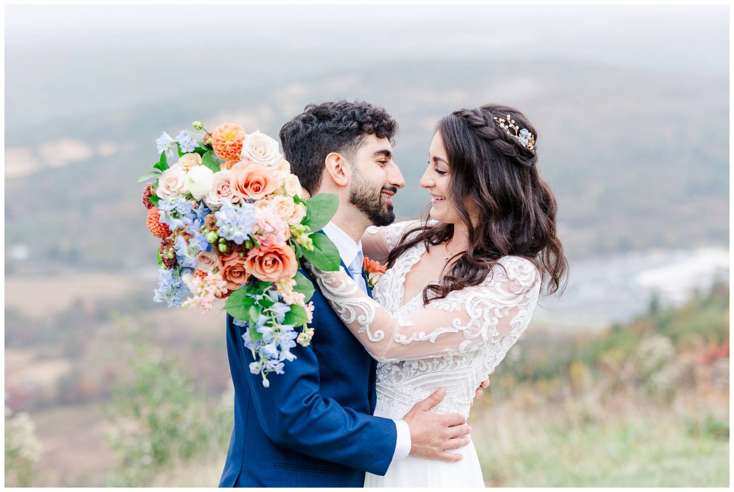 Romantic wedding portraits with coral and blue floral bouquet against mountain scenery.