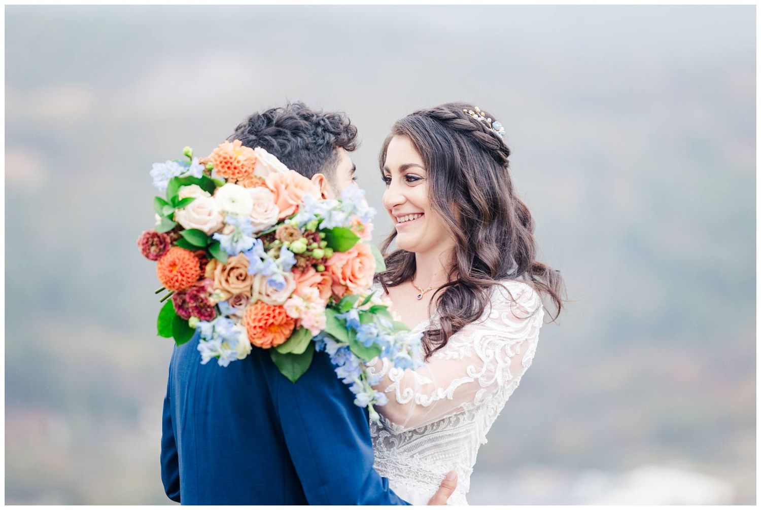 Elegant bridal bouquet featuring coral and white flowers with greenery against mountain backdrop.