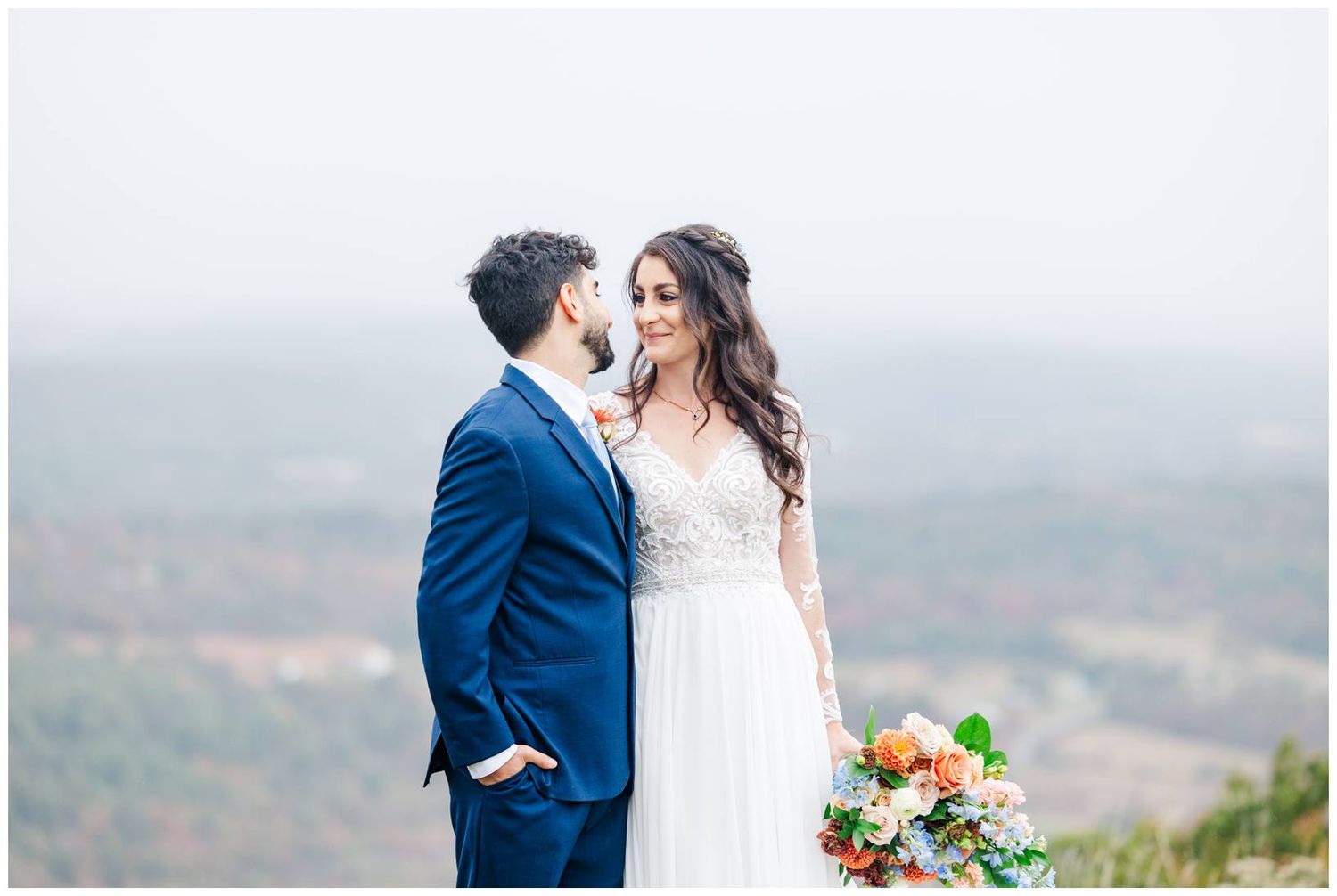 A romantic wedding portrait of a couple against a misty mountain landscape.