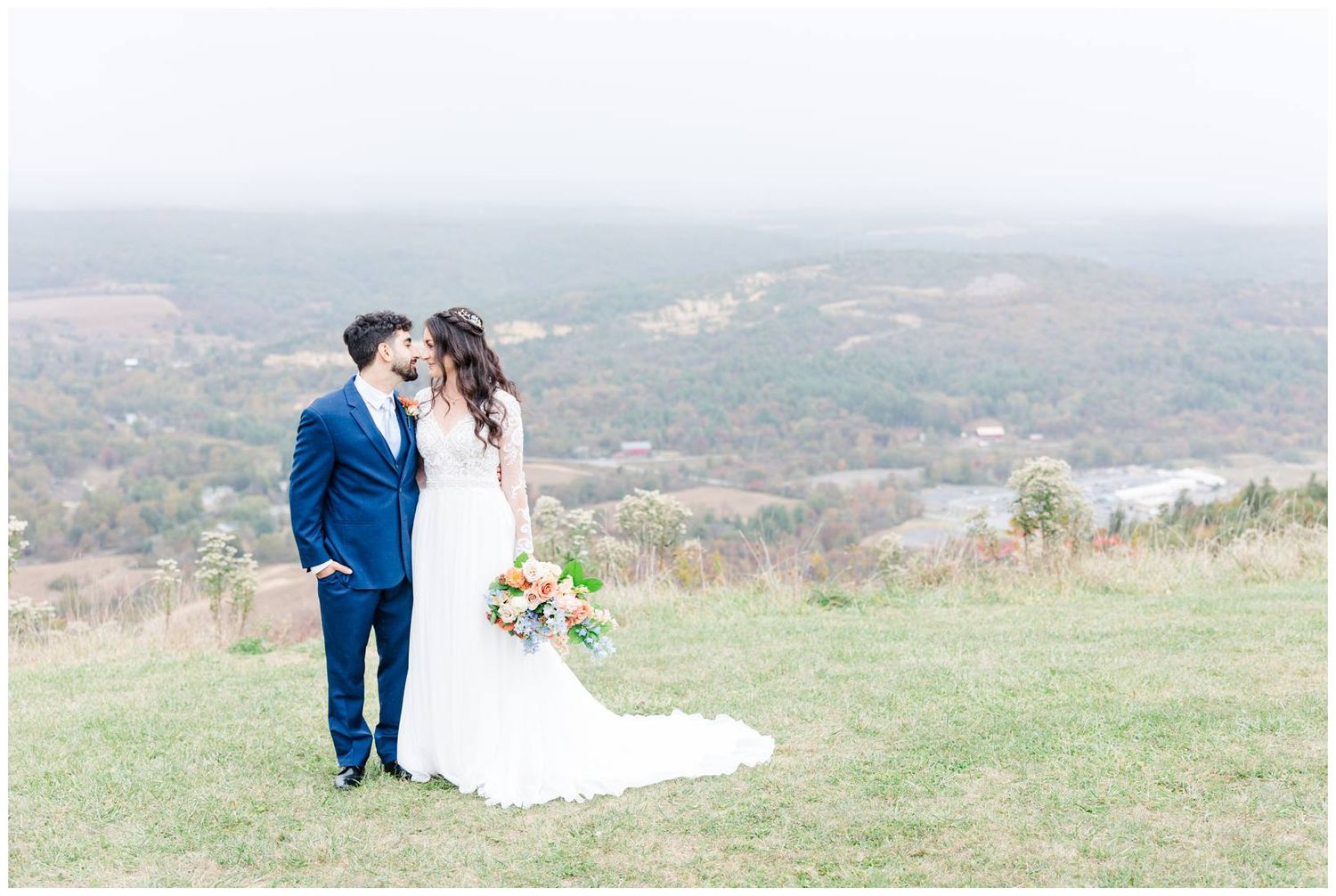 A couple shares an intimate moment on a hilltop with sweeping valley views.