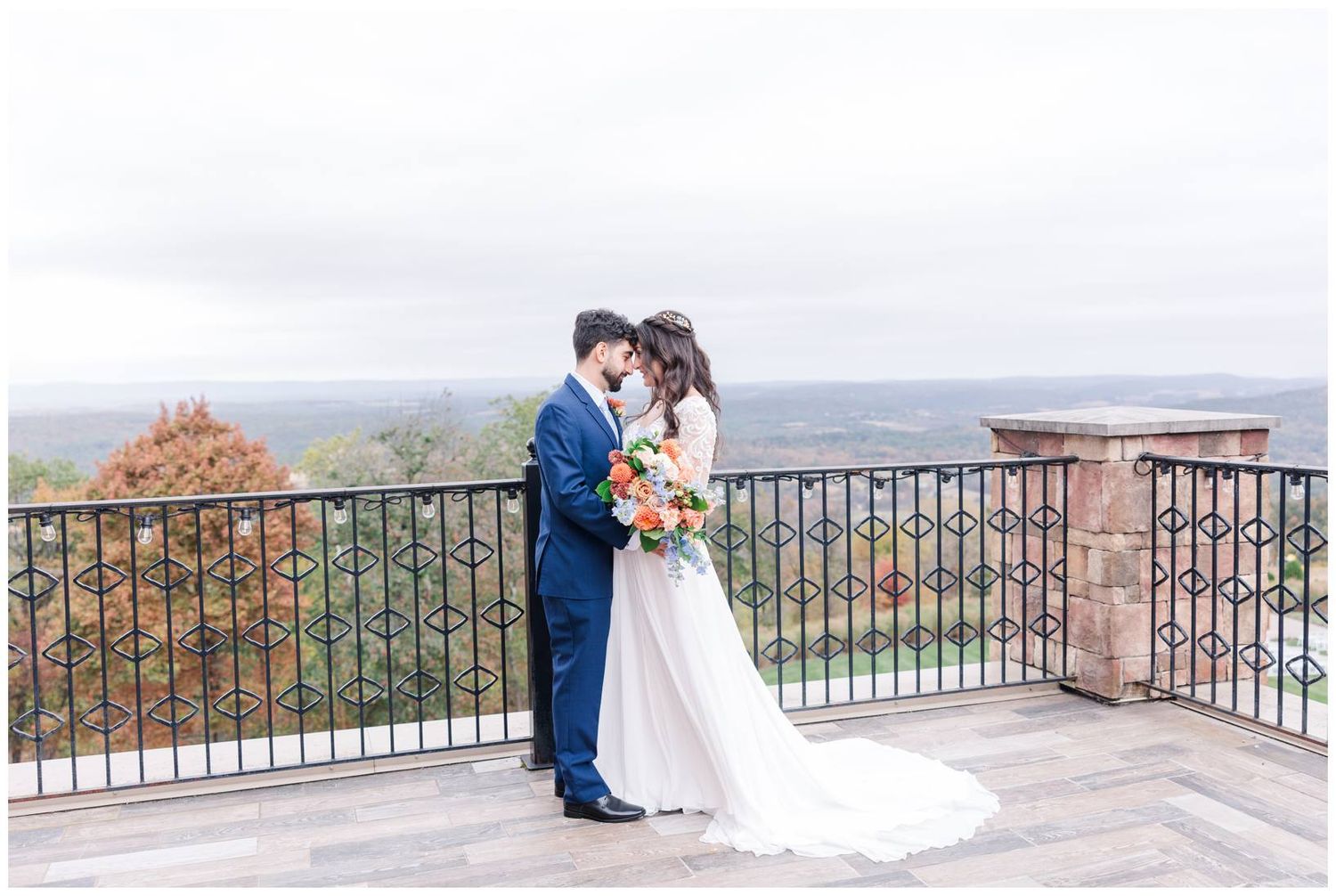 Wedding couple shares romantic moment on stone balcony overlooking misty mountain valley.