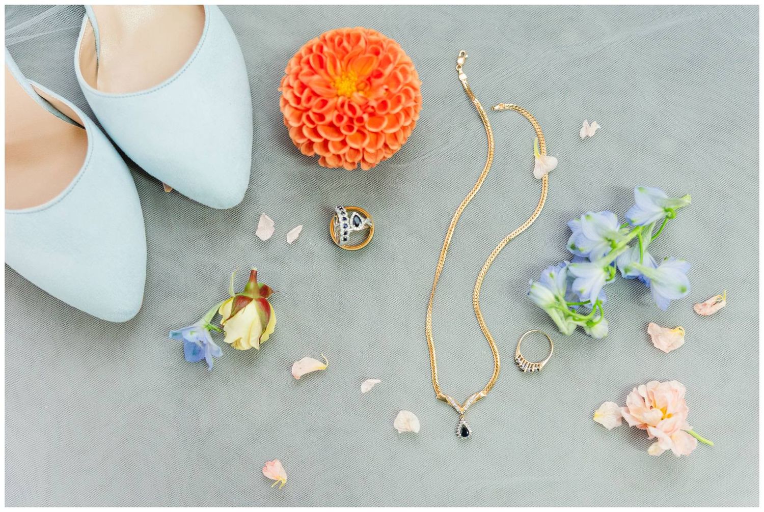 Wedding detail shot featuring light blue heels, coral flowers, and delicate jewelry on a grey surface.