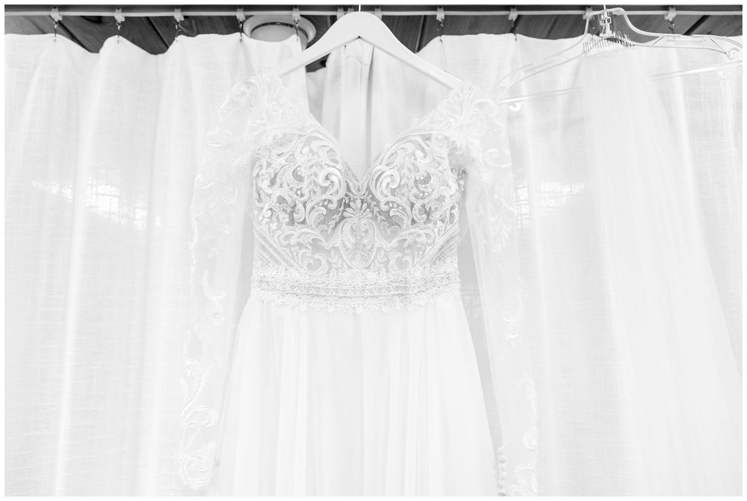 A delicate white lace wedding dress with intricate beading hangs against a light backdrop.