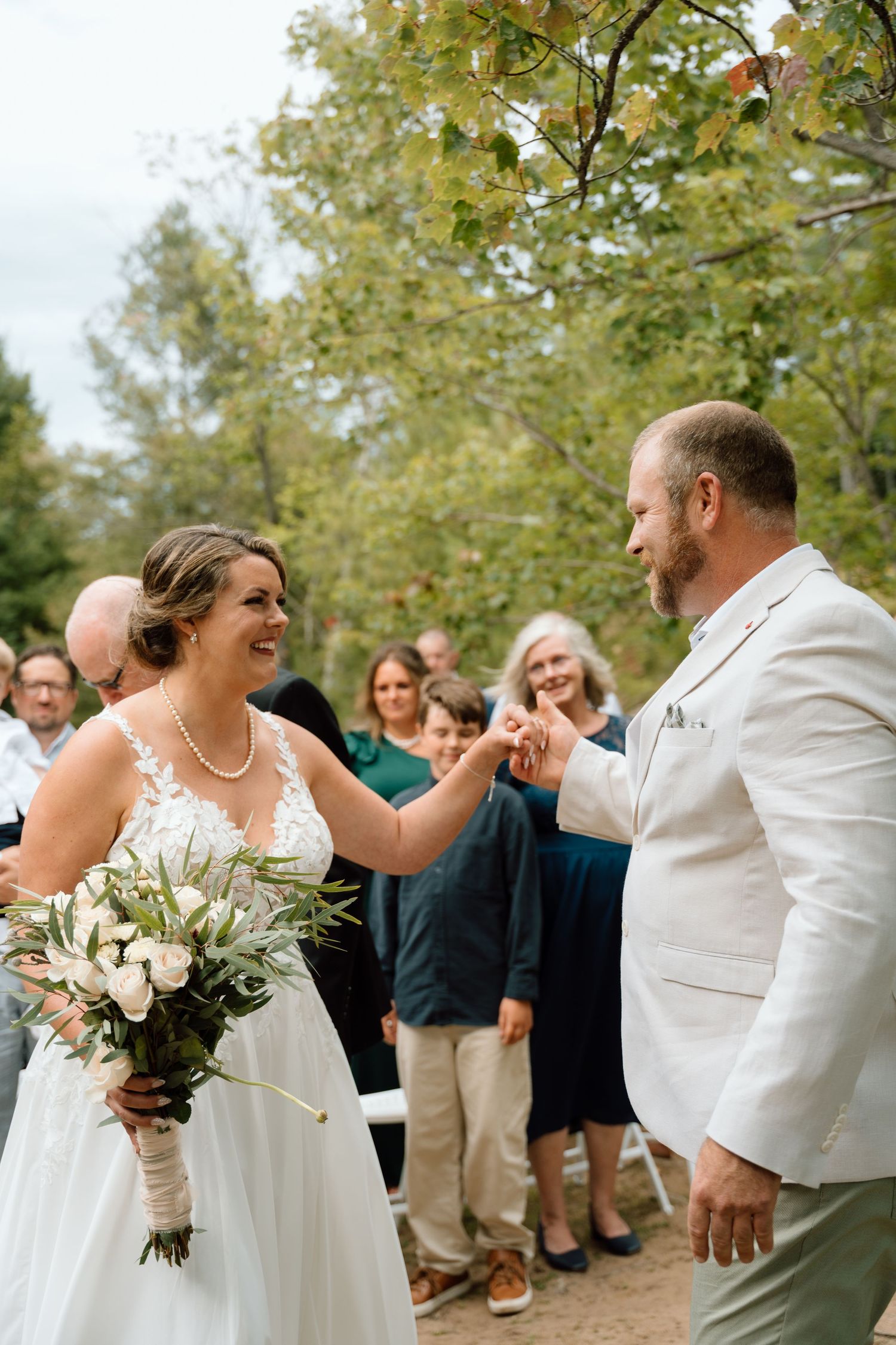A couple shares a joyful dance moment at an outdoor wedding celebration surrounded by guests and greenery.