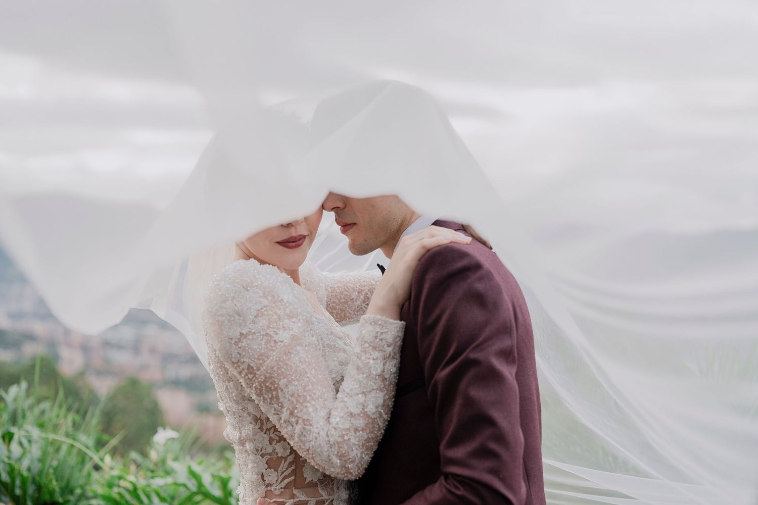Romantic wedding portrait with flowing veil against mountain landscape.