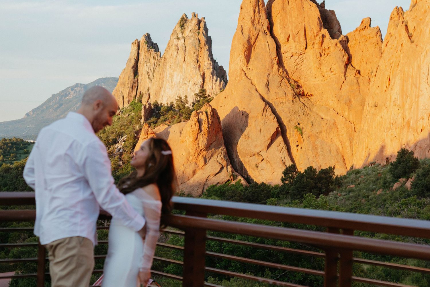 A couple in white attire shares a romantic moment against the backdrop of majestic red rock formations at sunset.