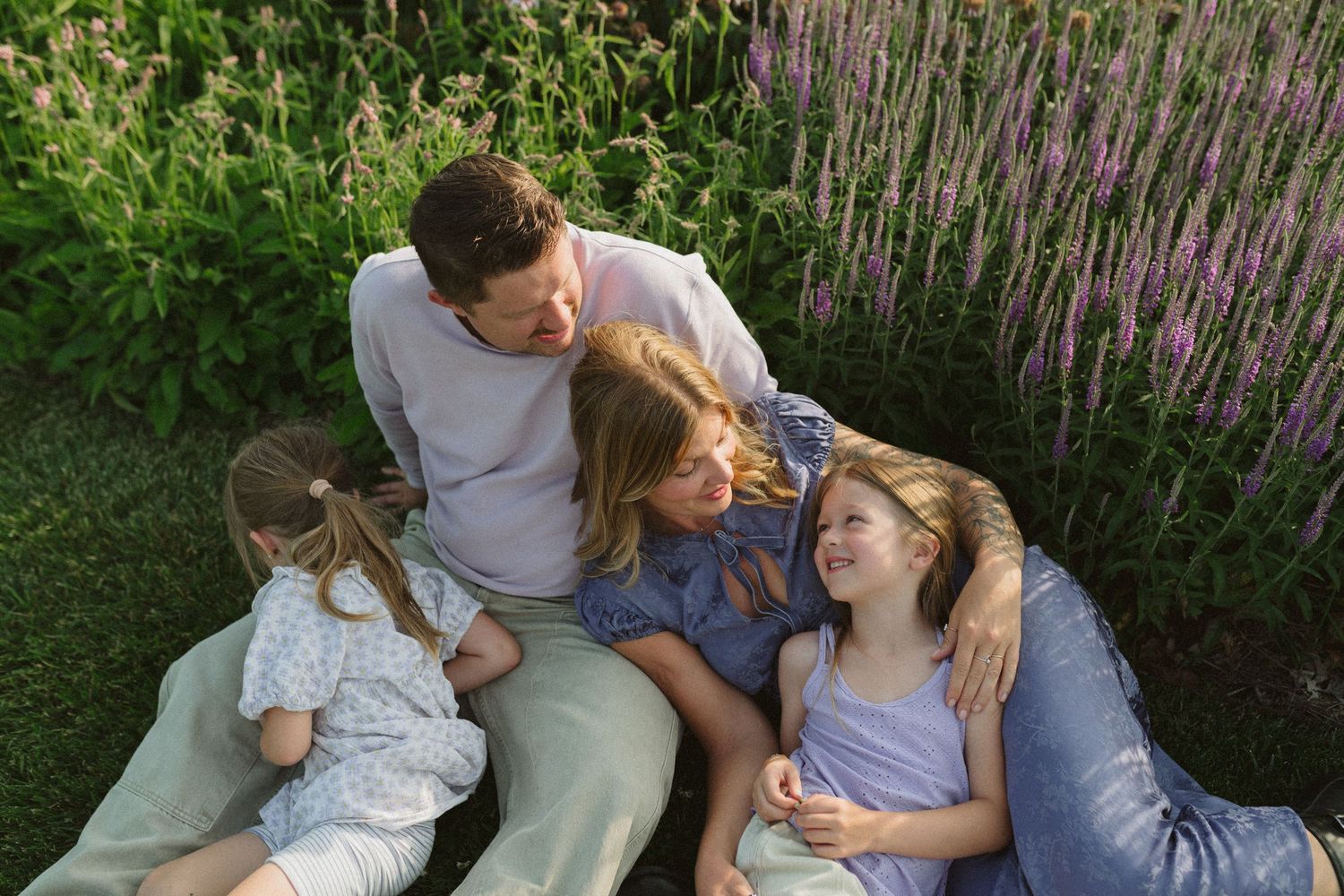 A couple shares intimate moments in a garden with purple flowers blooming in the background.