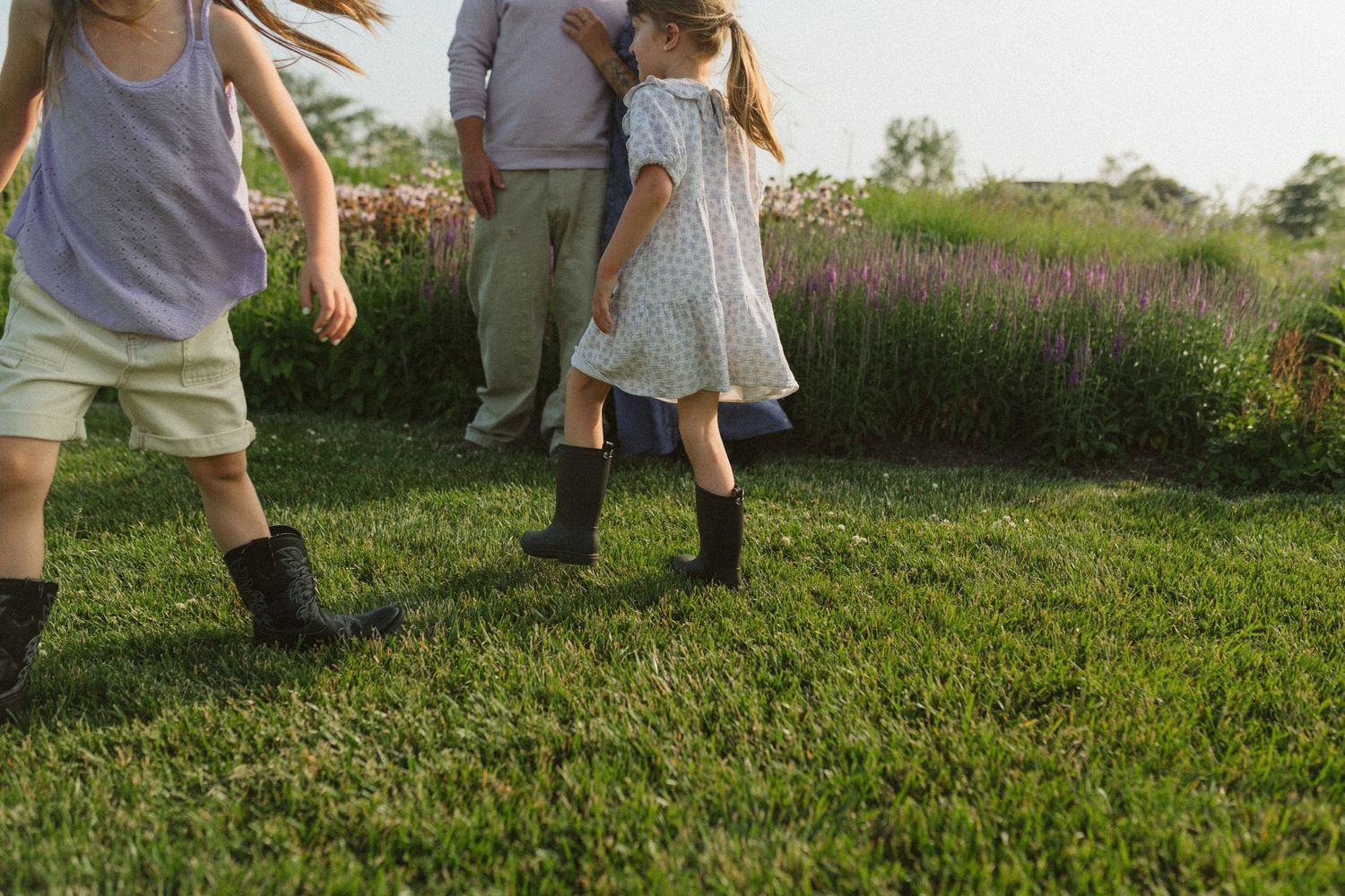 Kids playing and running through a lush green field at sunset.