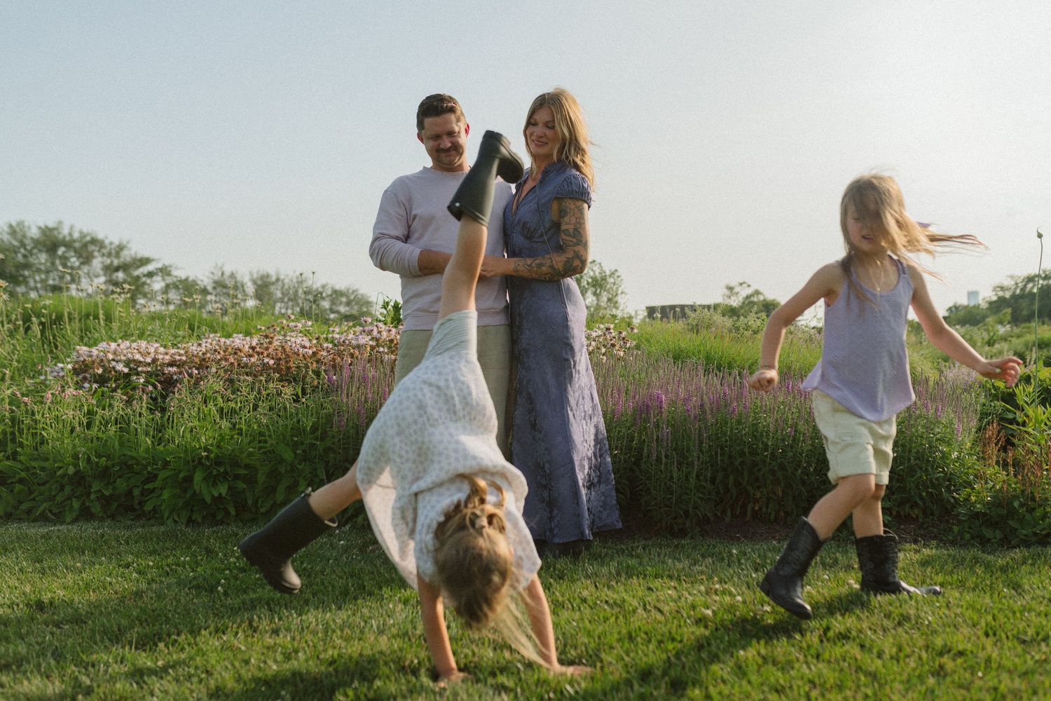 People in white outfits walking through a lush green field with wildflowers on a sunny summer day.