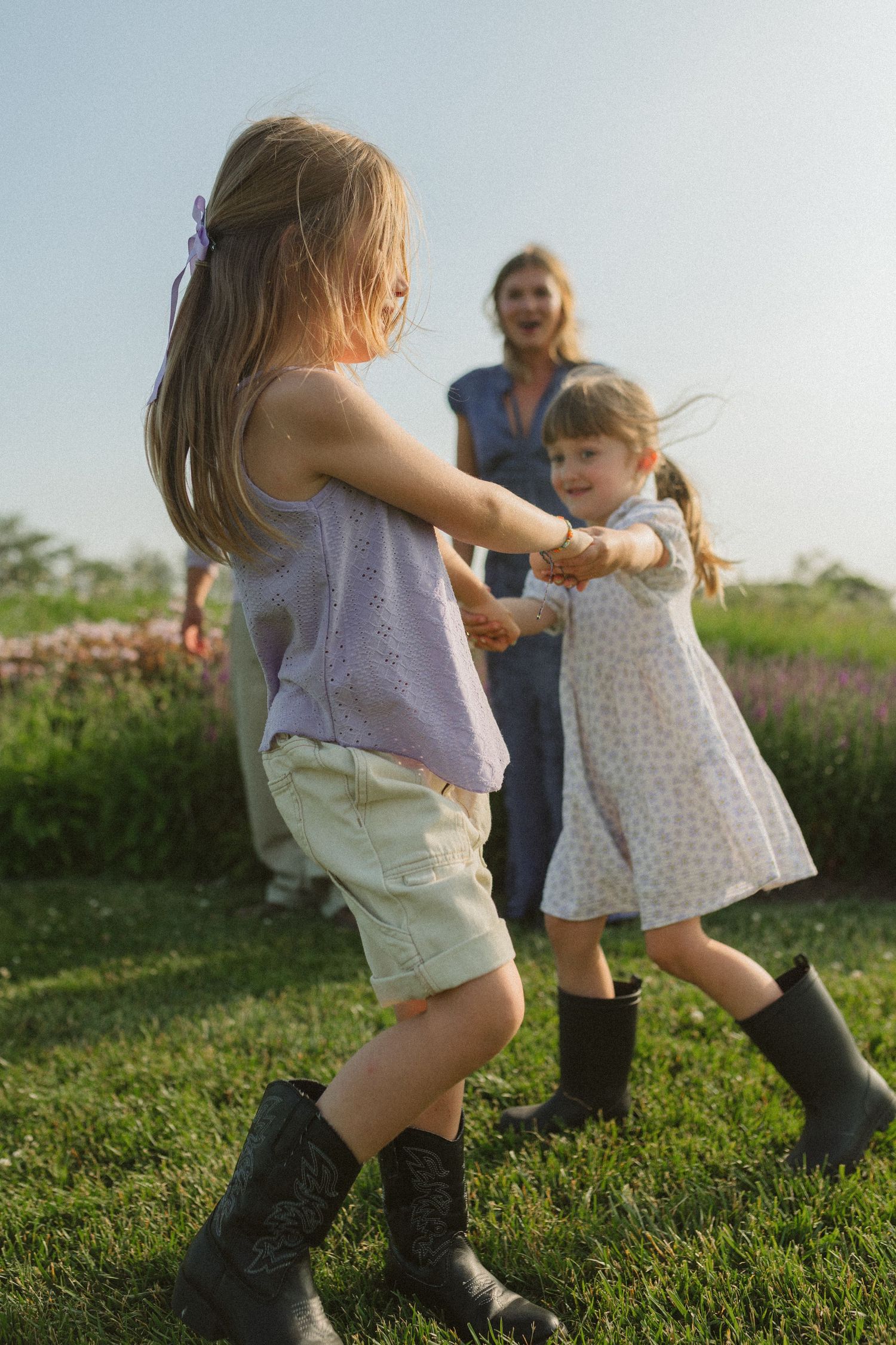 People holding hands and spinning in circles on a sunny hillside with wildflowers in the background.
