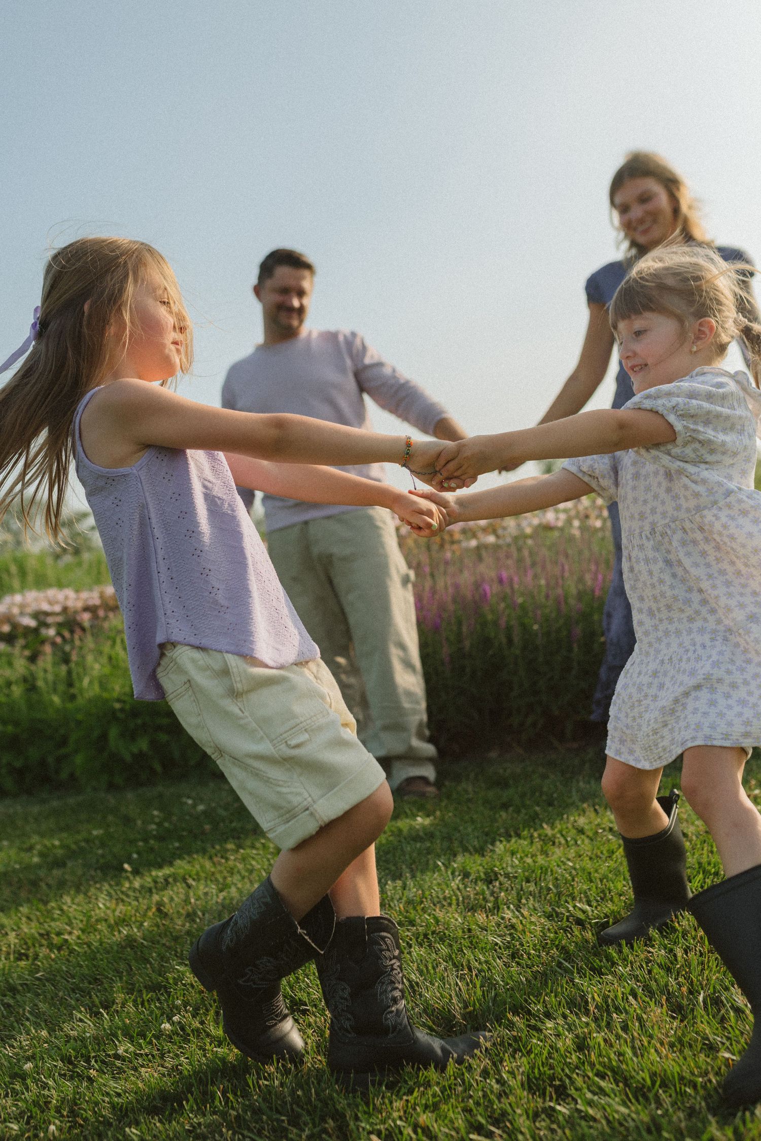 People holding hands and spinning in a circle on a grassy hillside at sunset.