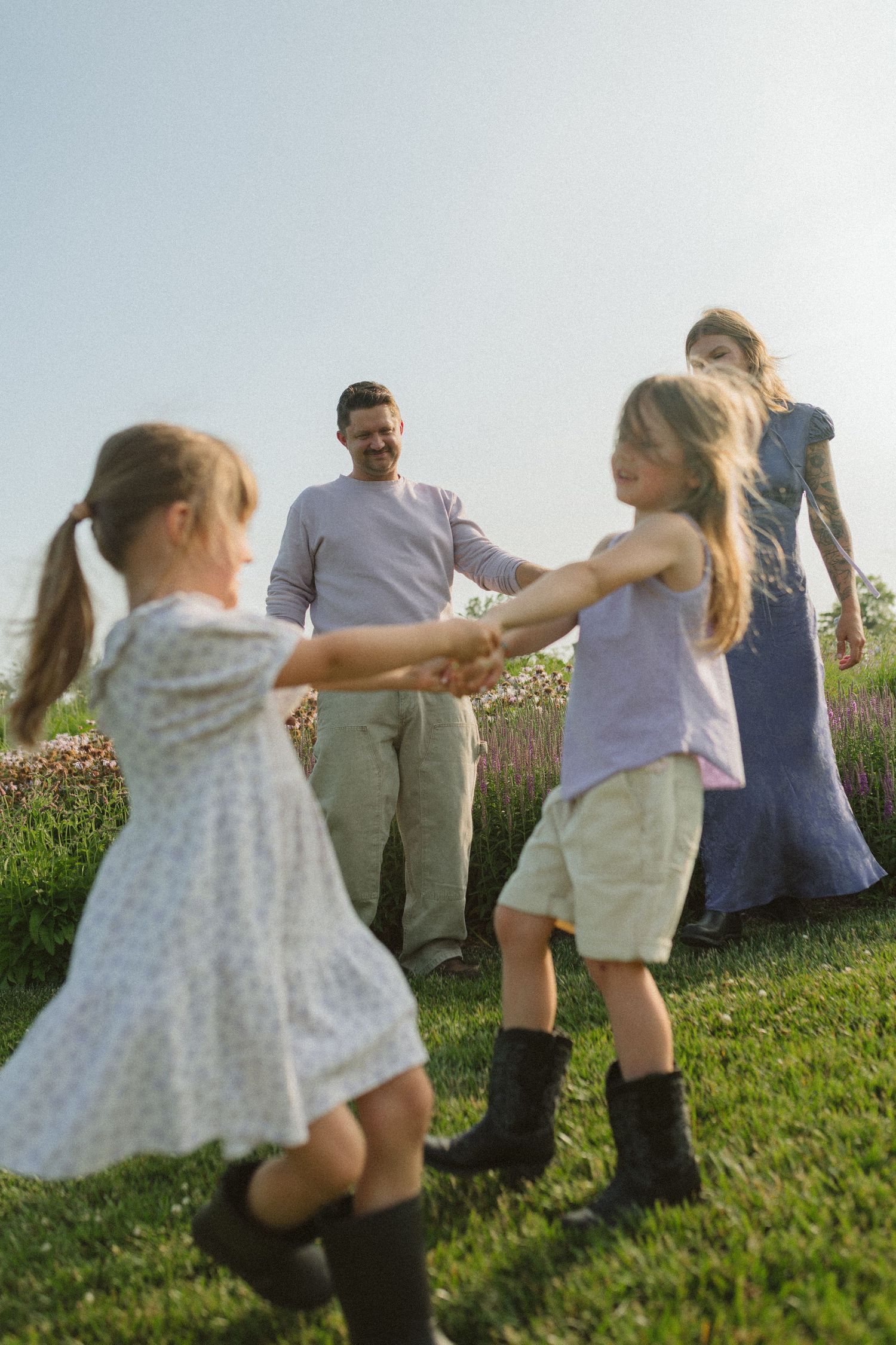 Children running and playing on a grassy slope with blooming flowers in the background.