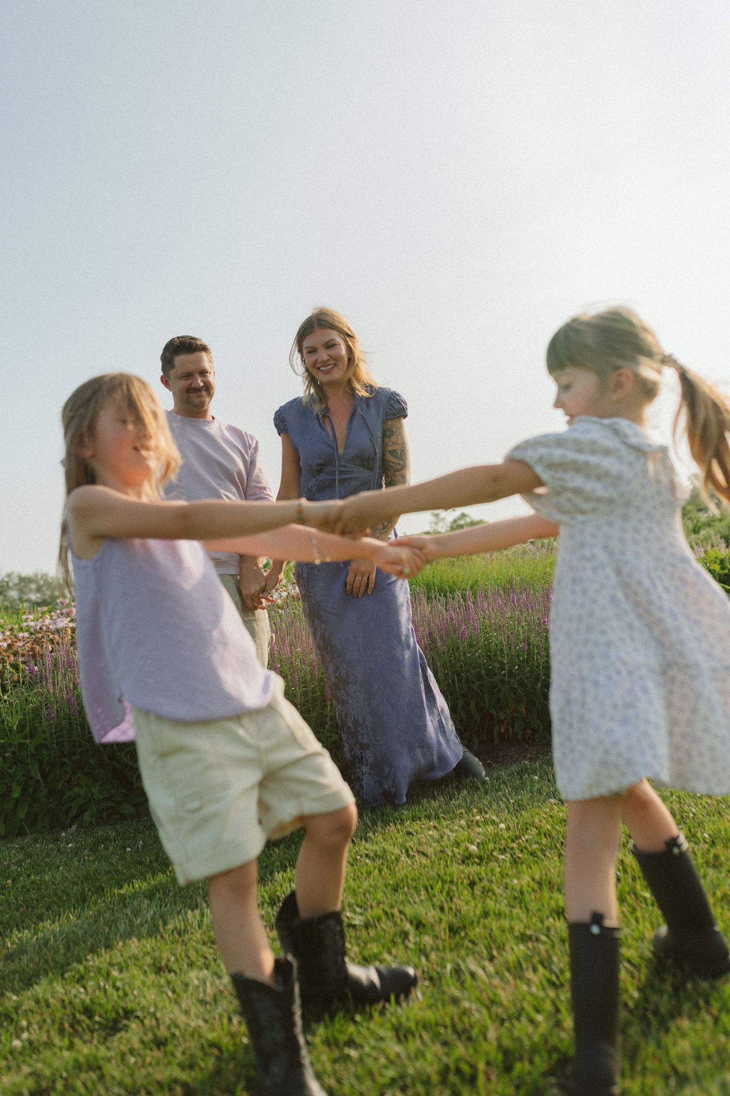 Dancing and twirling together on a grassy slope with summer flowers blooming nearby.