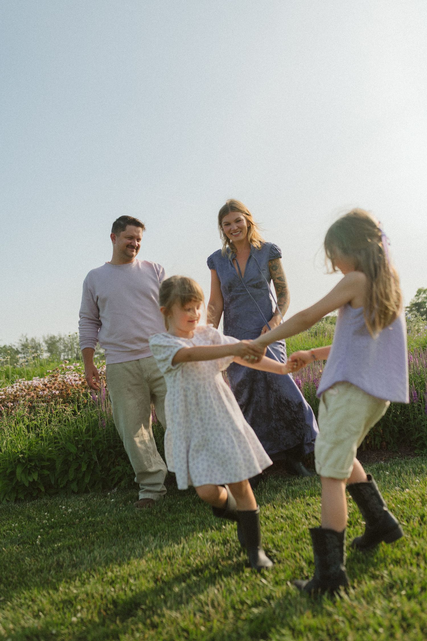Family playing and running together on a grassy hillside during golden hour sunset.