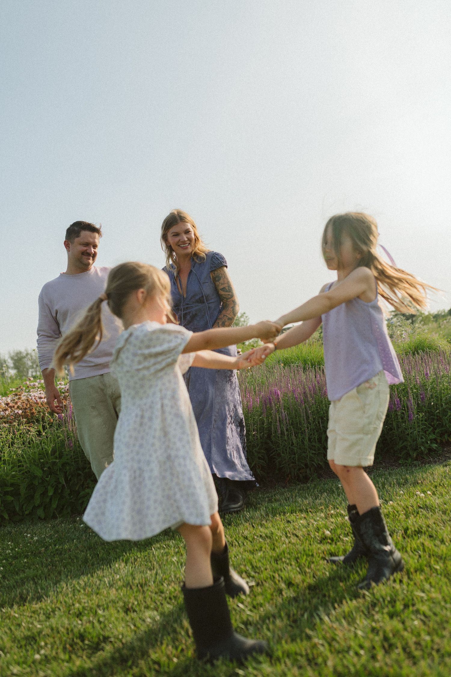 People dance and twirl on a grassy hill with wildflowers in the background at sunset.