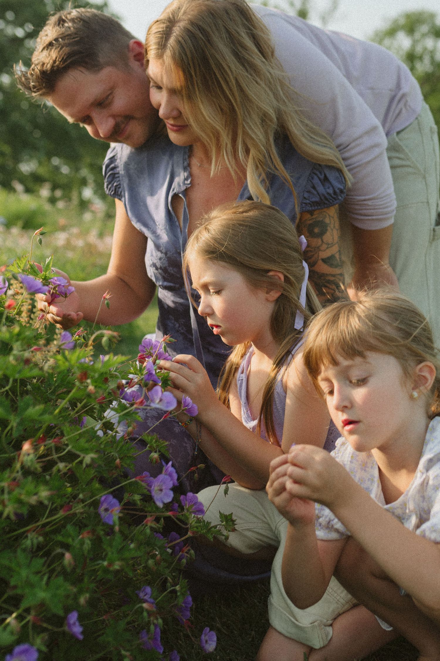 A group leans in close together to smell and examine purple flowers growing in a garden.